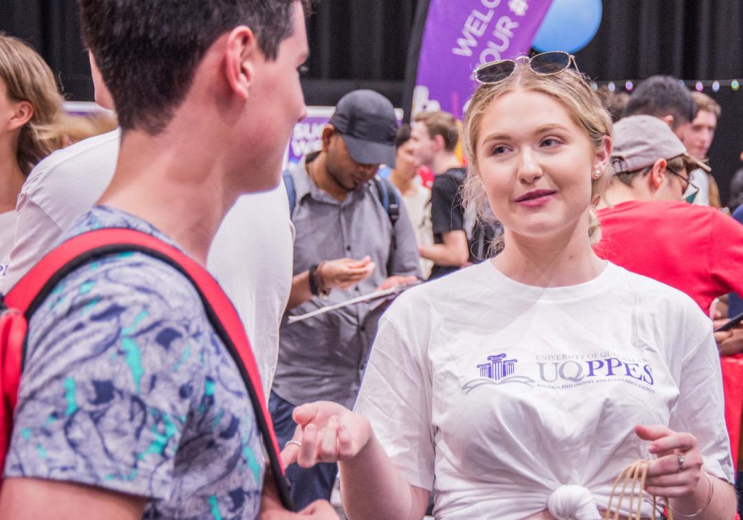 Student wearing UQ PPE Society t-shirt talking to another student.