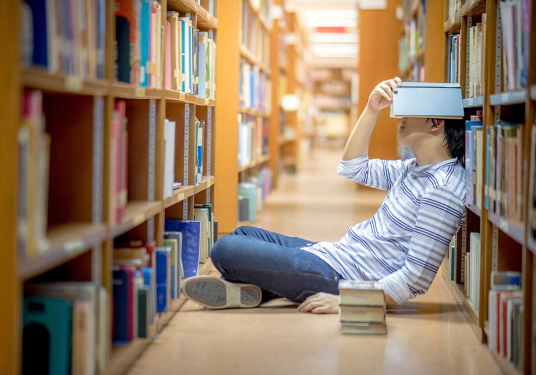 student sitting in library frustrated surrounded by books