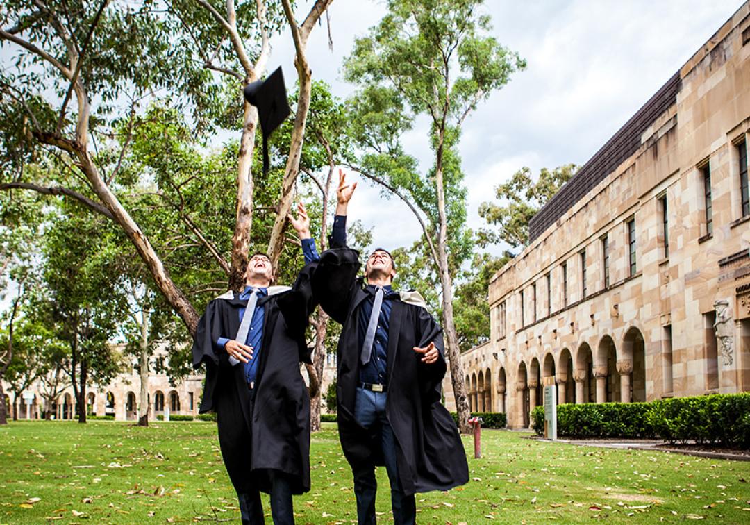 2 graduates throwing their caps in the air in the Great Court.