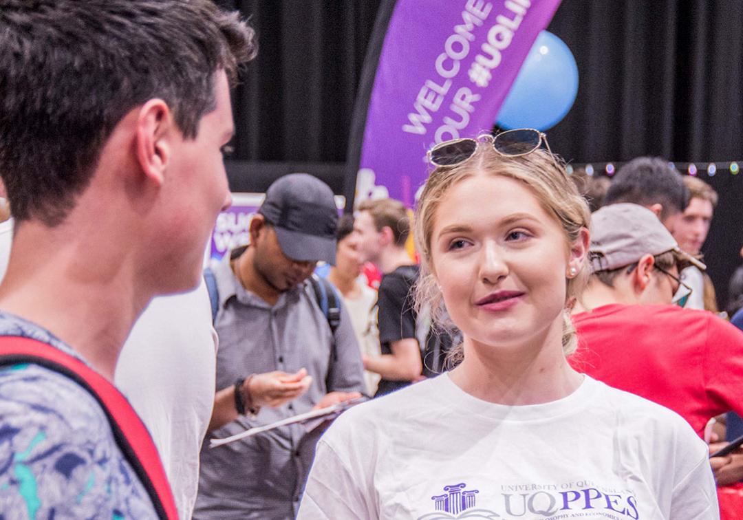 Student wearing UQ PPE Society t-shirt talking to another student.