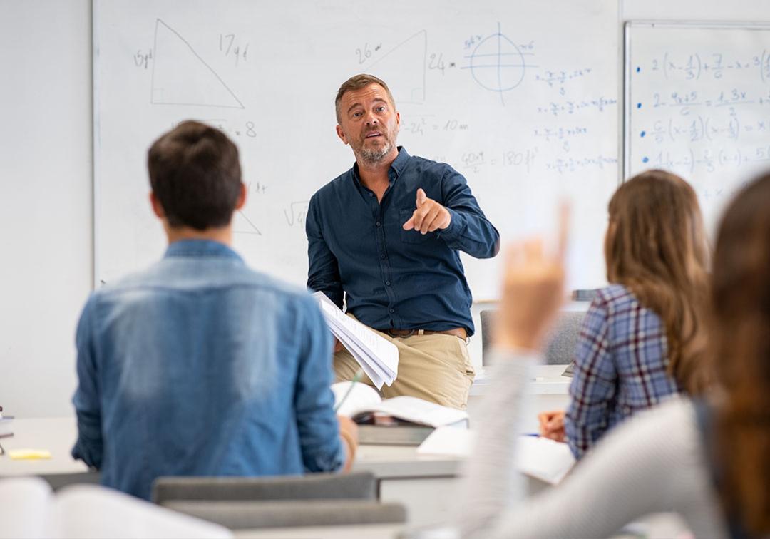 Teacher pointing to student with raised hand in classroom