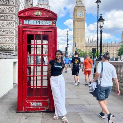 Esandi Kalugalage stands in front of a red phone box on a street in London with Big Ben in the background