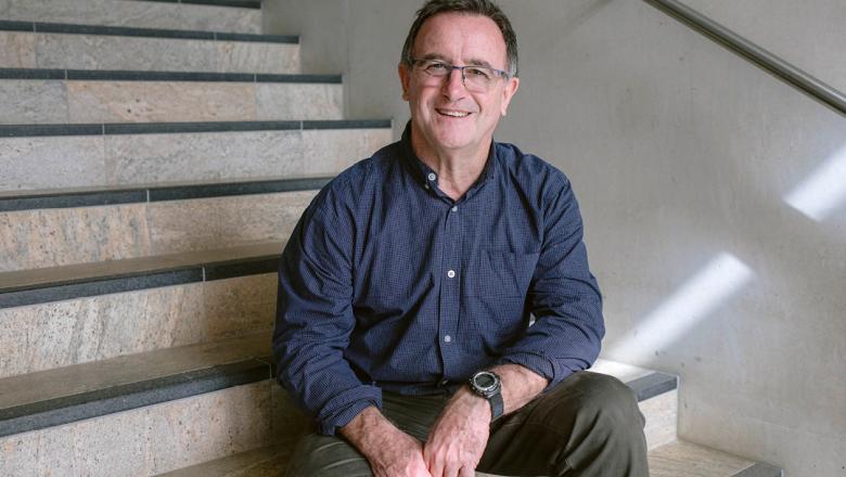 Associate Professor Ron Johnstone sits on a stone staircase smiling