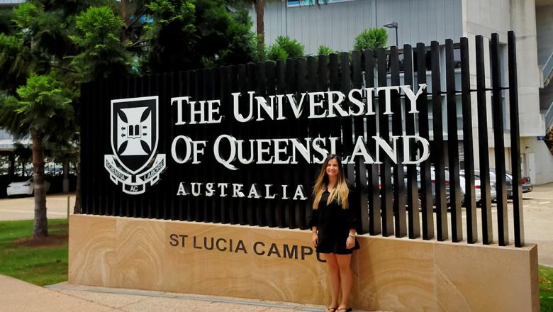 Student with long hair standing front of The University of Queensland signage