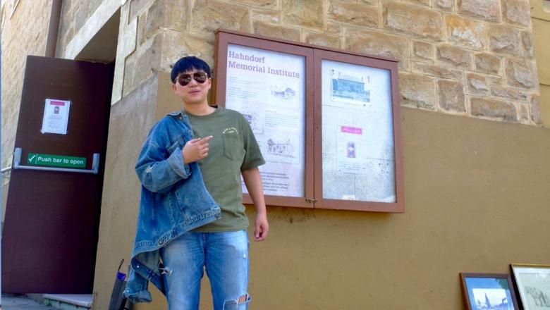 International student in sunglasses standing infront of stone wall with planning boards behind him. 