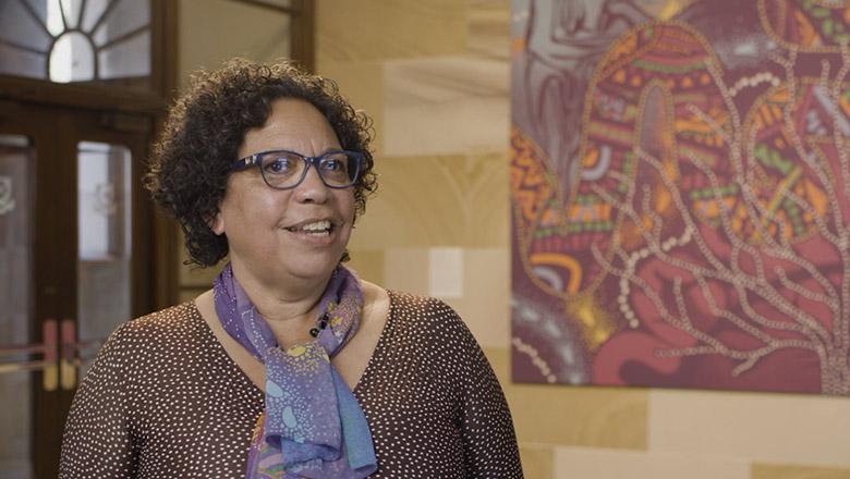 Sandra Phillips stands in front of Indigenous artwork