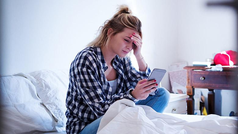 distressed teen in bedroom looking at phone
