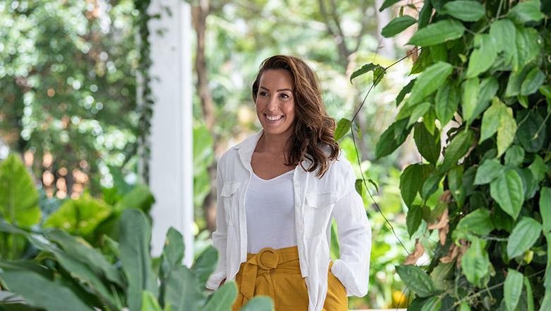 Natalie Craig stands with her hands in her pockets, smiling amongst green plants