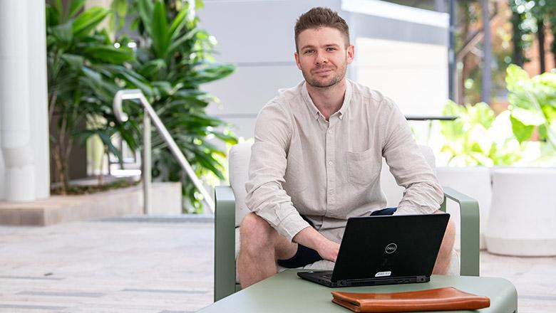 Sam Hislop-lynch sits with a laptop outside UQ's Student central
