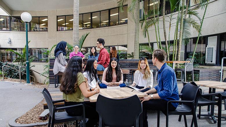 UQ psychology students sit around a table with workbooks, in discussion with one another