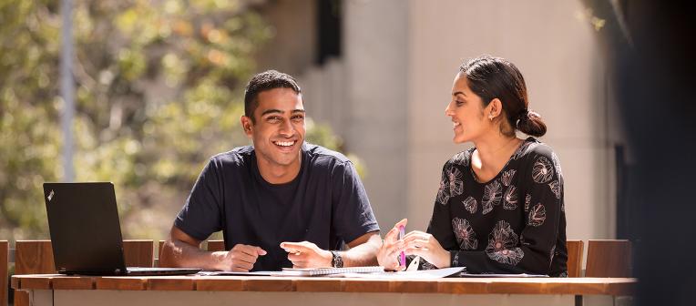 Male and female student sitting outside smiling. 