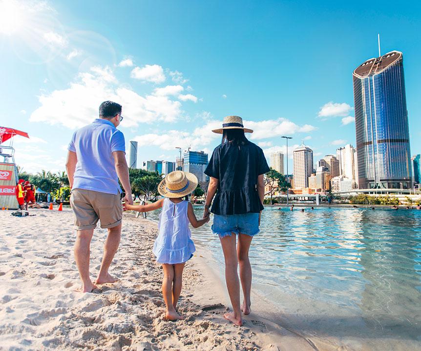 A family of three walk together at Streets Beach, South Bank in Brisbane.